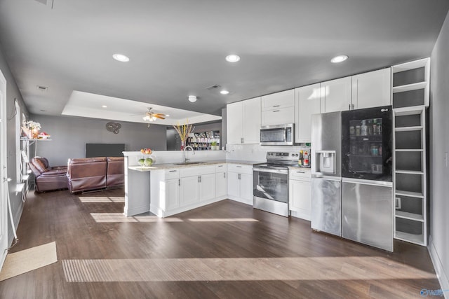 kitchen with appliances with stainless steel finishes, dark hardwood / wood-style floors, white cabinetry, sink, and kitchen peninsula