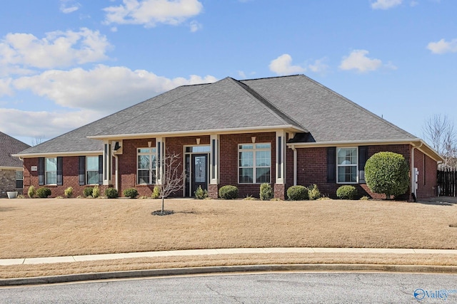 view of front of property featuring brick siding, roof with shingles, and a front yard