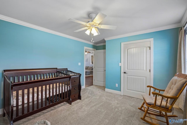 carpeted bedroom with a crib, a ceiling fan, baseboards, and crown molding