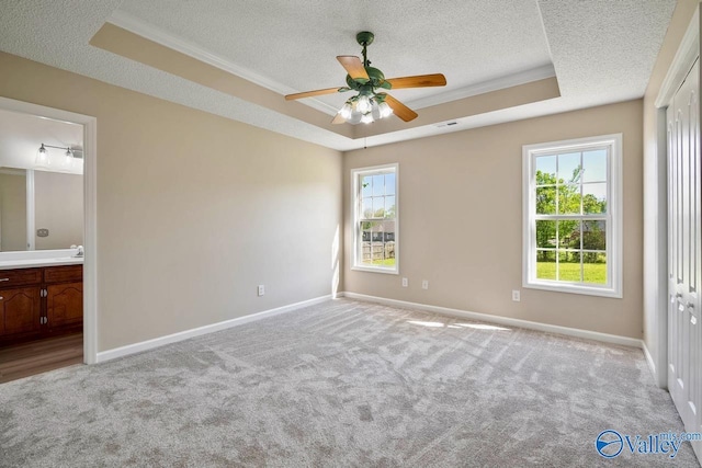 unfurnished bedroom featuring a tray ceiling, a textured ceiling, baseboards, carpet floors, and connected bathroom