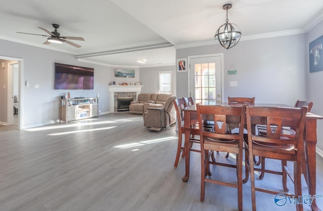 dining room with wood finished floors, baseboards, a fireplace, ornamental molding, and ceiling fan with notable chandelier