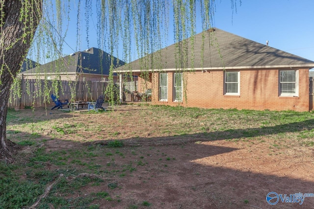 rear view of property featuring fence, brick siding, and a fire pit