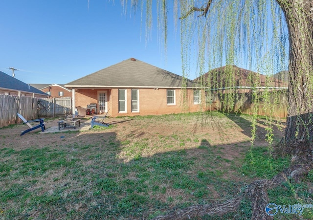 back of property with a lawn, a fenced backyard, an outdoor fire pit, brick siding, and a patio area