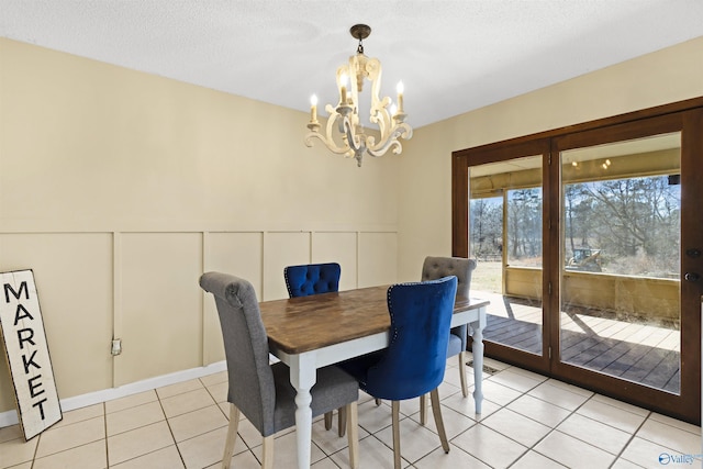 dining area with a notable chandelier, a decorative wall, wainscoting, light tile patterned flooring, and a textured ceiling