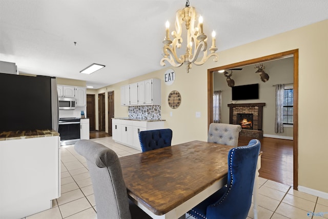 dining area featuring light tile patterned flooring, a fireplace, baseboards, and an inviting chandelier