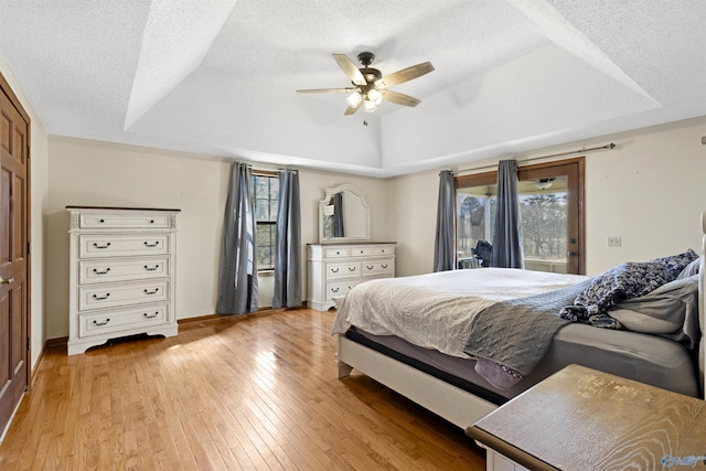 bedroom with a textured ceiling, light wood-type flooring, a raised ceiling, and a ceiling fan