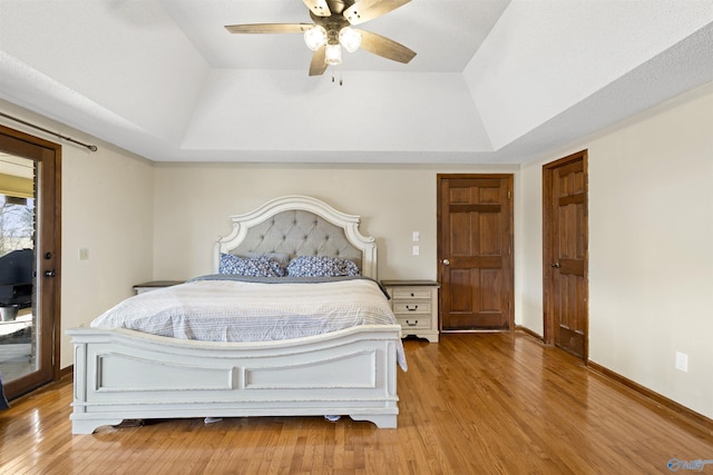 bedroom featuring baseboards, ceiling fan, access to exterior, a tray ceiling, and light wood-type flooring