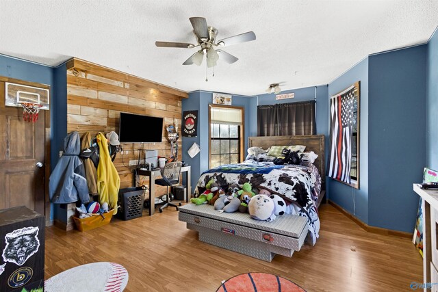 bedroom featuring ceiling fan, wooden walls, a textured ceiling, wood finished floors, and baseboards