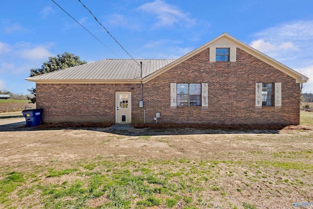 back of property with metal roof, a lawn, and brick siding