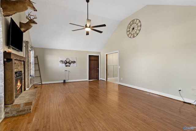 unfurnished living room with baseboards, ceiling fan, wood finished floors, a brick fireplace, and high vaulted ceiling