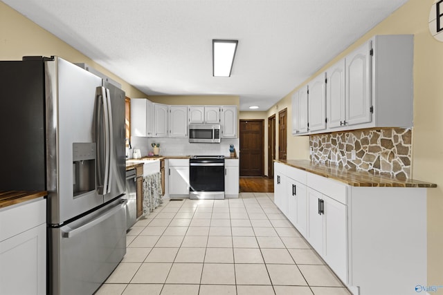 kitchen featuring stainless steel appliances, light tile patterned flooring, white cabinetry, and decorative backsplash