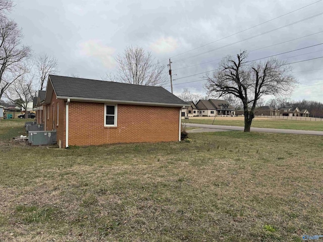 view of side of home with a yard, brick siding, and a shingled roof