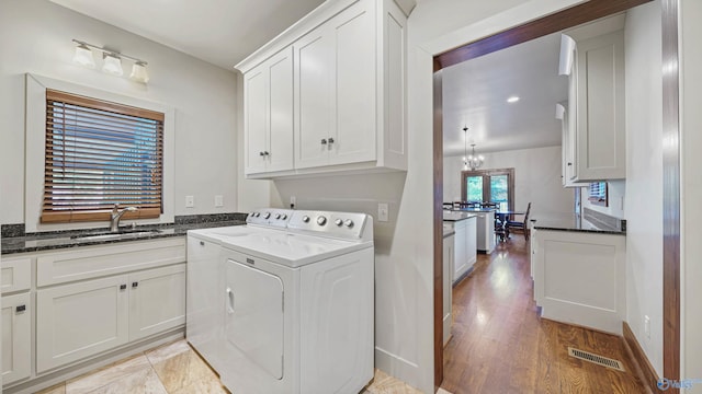 laundry room featuring sink, cabinets, light wood-type flooring, washer and dryer, and a chandelier