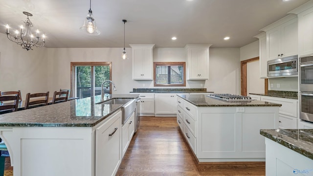 kitchen with white cabinets, stainless steel appliances, wood-type flooring, and a center island with sink