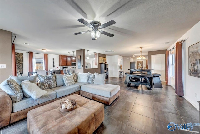 living room with a textured ceiling, dark tile patterned floors, and ceiling fan with notable chandelier