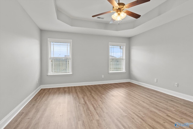 unfurnished room featuring a tray ceiling, a healthy amount of sunlight, and light hardwood / wood-style floors