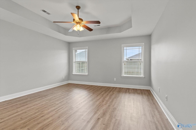 unfurnished room featuring ceiling fan, a healthy amount of sunlight, a raised ceiling, and light wood-type flooring