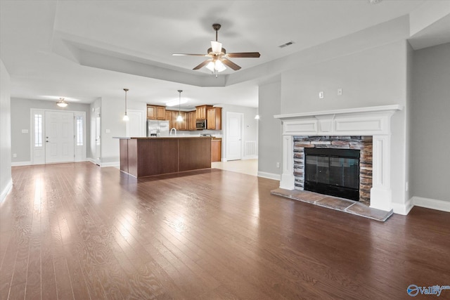 unfurnished living room featuring hardwood / wood-style floors, a stone fireplace, and ceiling fan