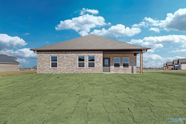 back of house with a shingled roof, a lawn, and brick siding