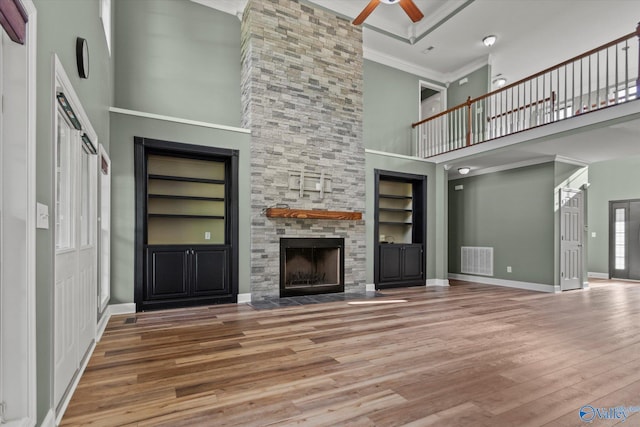 123 Coyote Creek Rd, Meridianville, AL 35759 - unfurnished living room featuring a towering ceiling, built in shelves, ceiling fan, wood finished floors, and a fireplace