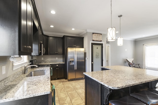 kitchen with hanging light fixtures, stainless steel fridge, light stone counters, a kitchen island, and sink