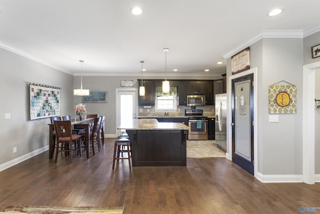 kitchen featuring a center island, light stone counters, pendant lighting, crown molding, and appliances with stainless steel finishes