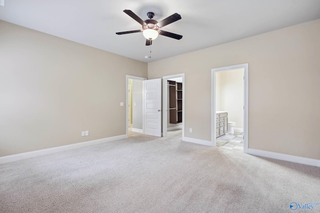 unfurnished bedroom featuring ensuite bathroom, a spacious closet, light carpet, a closet, and ceiling fan