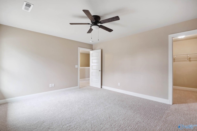 unfurnished bedroom with ceiling fan, a walk in closet, a closet, and light carpet