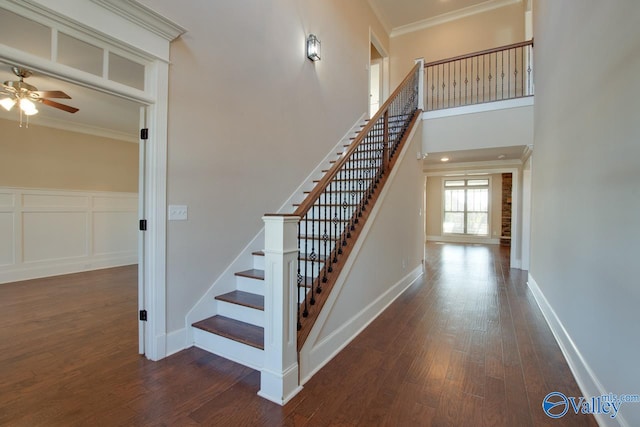 staircase featuring a high ceiling, hardwood / wood-style flooring, ceiling fan, and ornamental molding