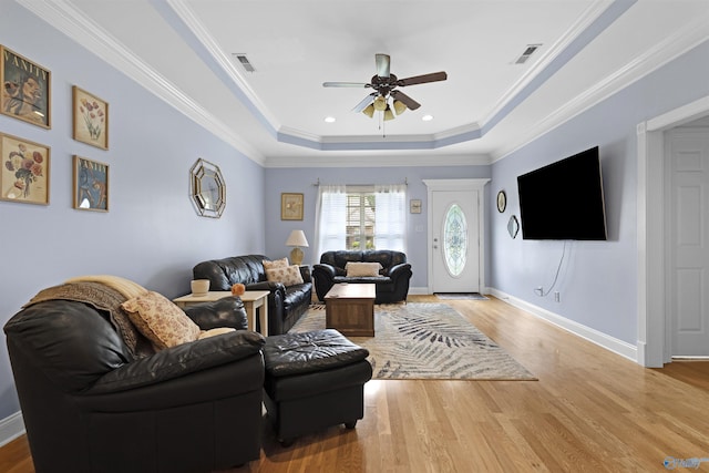 living area with a ceiling fan, a tray ceiling, visible vents, and wood finished floors