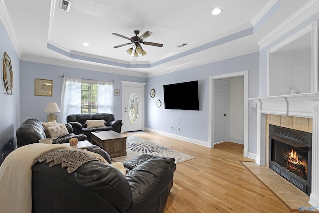 living room with a ceiling fan, visible vents, a tiled fireplace, light wood-type flooring, and a tray ceiling