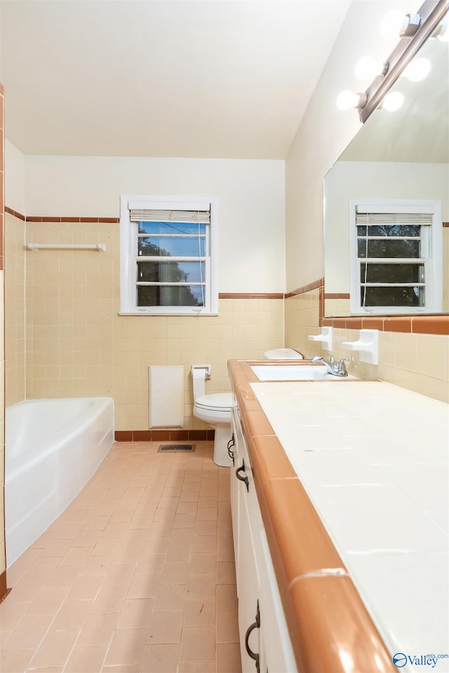 bathroom with vanity, toilet, a bathing tub, tile walls, and tile patterned flooring