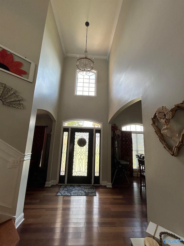 foyer with an inviting chandelier, a towering ceiling, crown molding, and dark hardwood / wood-style flooring