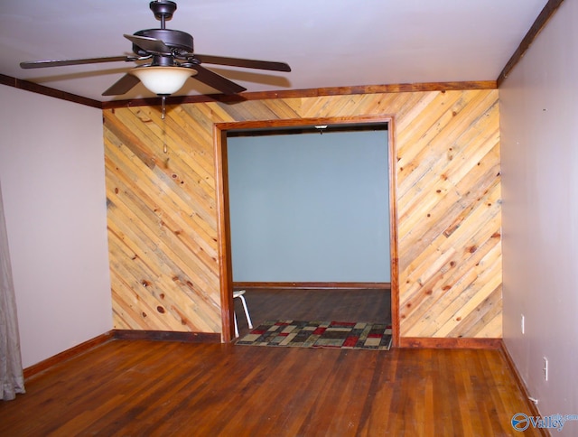 empty room with ornamental molding, ceiling fan, dark wood-type flooring, and wood walls