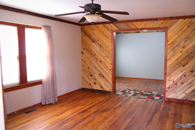 spare room featuring hardwood / wood-style floors, ceiling fan, plenty of natural light, and wood walls