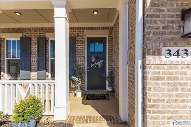 view of exterior entry with a porch and brick siding