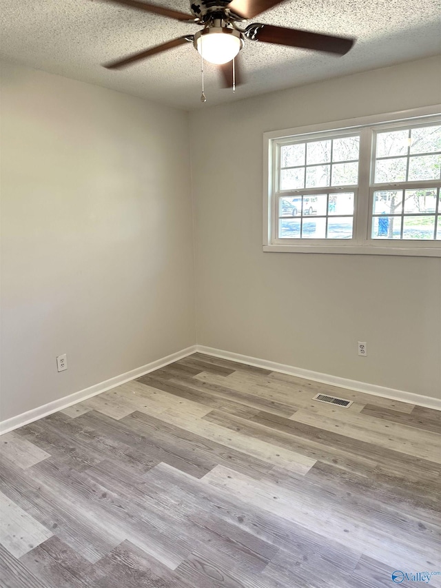 spare room with visible vents, baseboards, ceiling fan, a textured ceiling, and wood finished floors