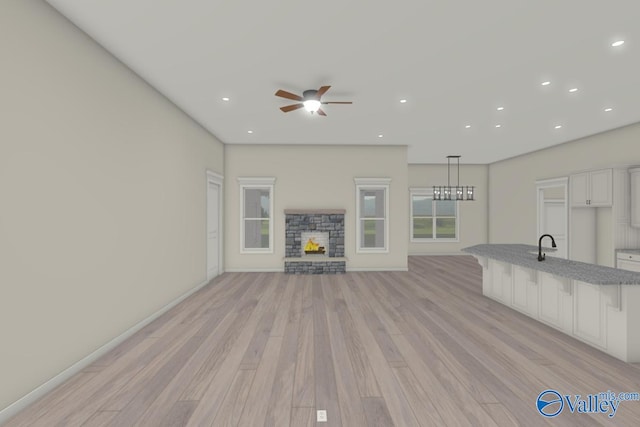 unfurnished living room featuring sink, a fireplace, light hardwood / wood-style floors, and ceiling fan