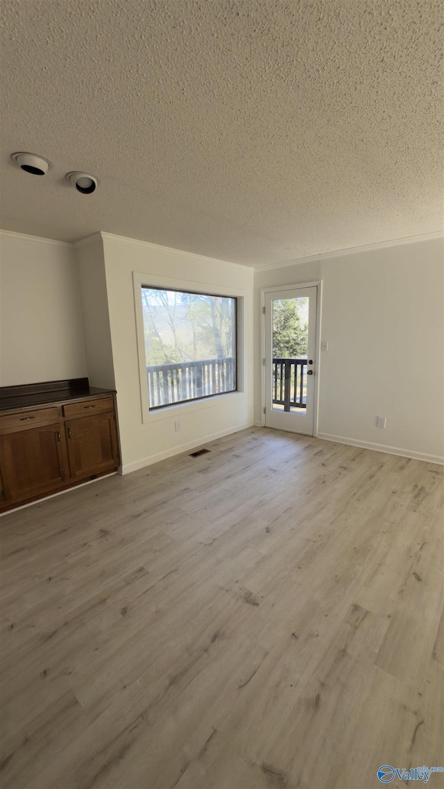 unfurnished living room with crown molding, a textured ceiling, and light wood-type flooring