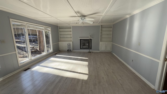 unfurnished living room featuring built in shelves, ceiling fan, crown molding, and hardwood / wood-style flooring