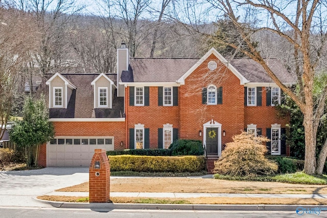 view of front facade with brick siding, driveway, a chimney, and an attached garage