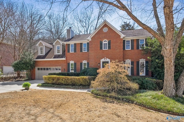 colonial house with an attached garage, brick siding, a chimney, and driveway