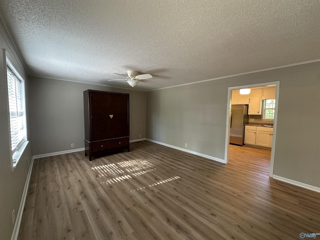 unfurnished bedroom with ornamental molding, a textured ceiling, freestanding refrigerator, and wood finished floors
