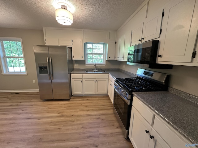 kitchen featuring a textured ceiling, white cabinets, a sink, appliances with stainless steel finishes, and dark countertops