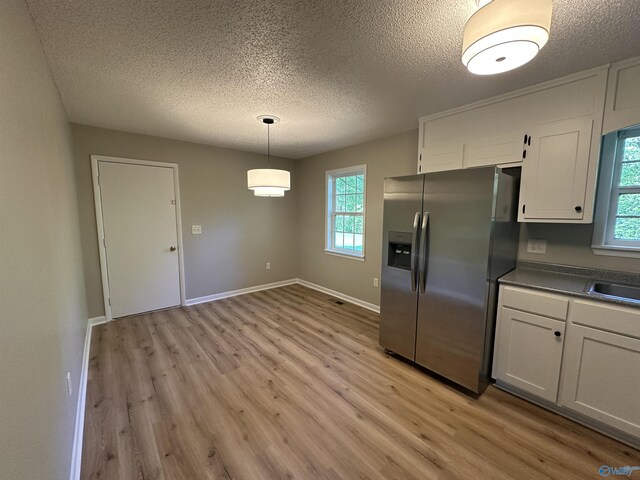 kitchen featuring stainless steel fridge, a textured ceiling, white cabinets, and light wood-style flooring