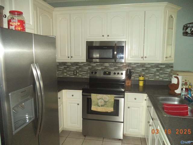 kitchen with dark countertops, light tile patterned floors, decorative backsplash, appliances with stainless steel finishes, and a sink