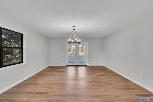 unfurnished dining area featuring light hardwood / wood-style flooring, french doors, and a notable chandelier