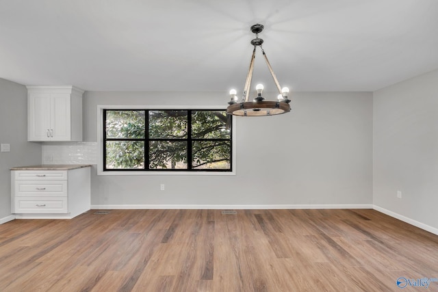 unfurnished dining area with a notable chandelier and light hardwood / wood-style flooring