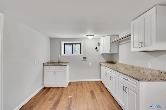 kitchen with white cabinetry, sink, light stone countertops, and light hardwood / wood-style flooring