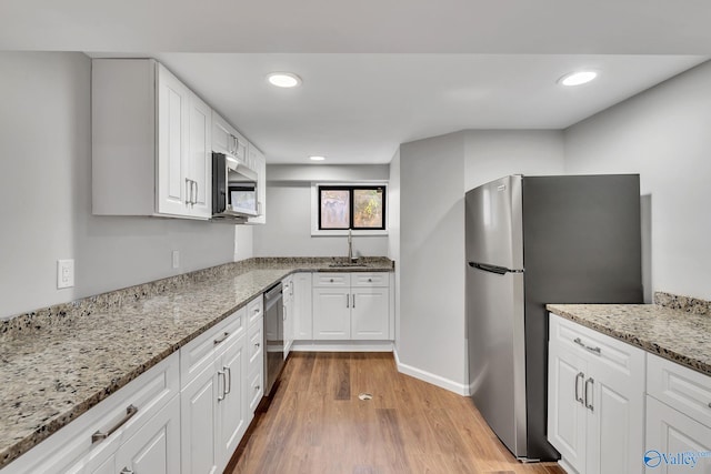 kitchen with white cabinets, light stone countertops, appliances with stainless steel finishes, and light hardwood / wood-style flooring